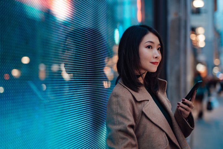 Young woman holding phone while waiting on a city street at night